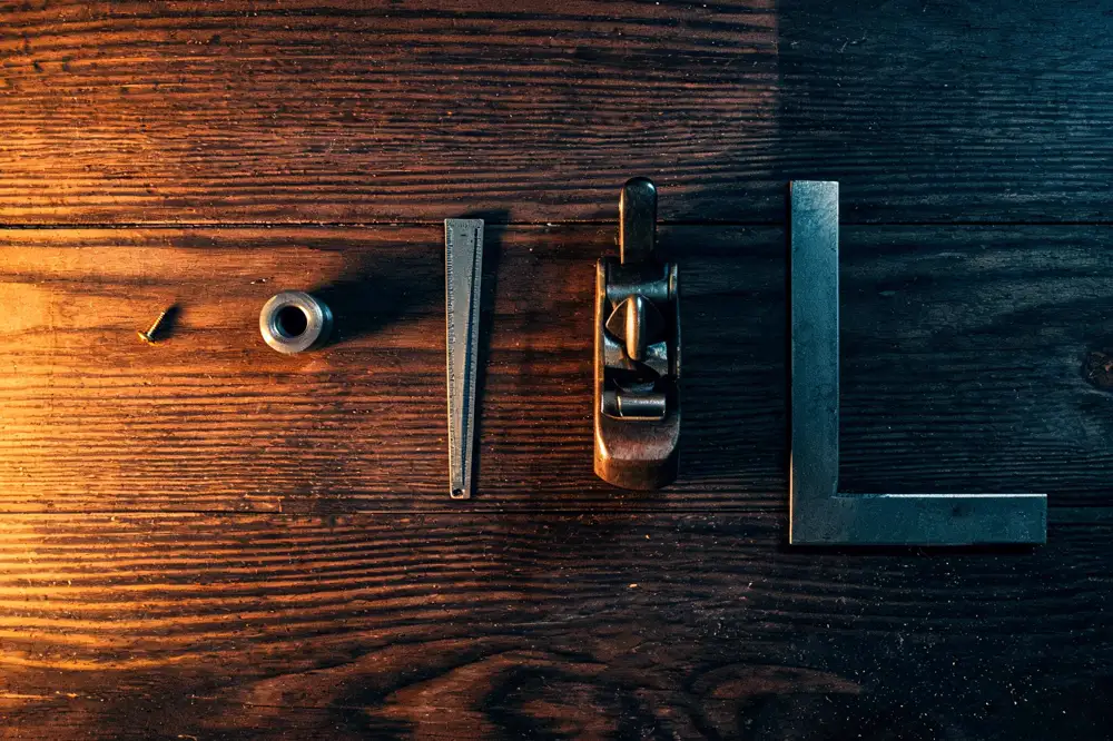 Five workshop objects of very different sizes — a screw, a bushing, a steel rule, a plane and an engineer's square — laid out on a bench with identical spacing between them.